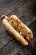 American hot dog with grilled sausage, deep-fried onions and pickled cucumbers on a rustic background