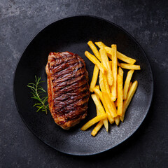 Beef Steak medium rare with French fries on a black plate. Grey background. Close up. Top view.