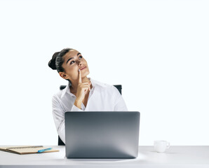 Thinking concept with pensive young woman looking up and trying to find best solution, sitting in front of modern laptop isolated on light wall background, closeup