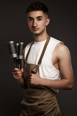 Wall Mural - Handsome man hairdresser in a working uniform with brushing combs in his hands.