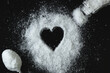 Heart made of salt, which is scattered on the table. Nearby is a metal spoon with salt and an open salt shaker with which salt is poured out