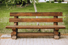Photo Of An Empty Wooden Brown Bench In The Park Against The Background Of Green Grass And Birch.
