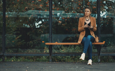 Woman with smartphone is waiting for bus at bus stop.