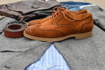 A pair of brown suede derby shoes, blue jeans, leather bag and belt with grey tweed blazer. Casual business outlook. Selective focus.