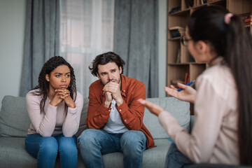 Wall Mural - Sad pensive young caucasian man and black female listened to psychiatrist in clinic interior