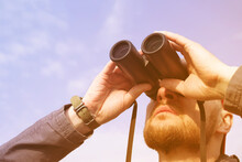 Young Man Looks Up Through Binoculars Against A Blue Sky, Close-up. Birdwatching