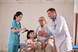 © tigercat_lpg - Professional Caucasian male doctor advises grandfather and grandchild, explains prescription with medical trainees at patient hospital bed, illness consultations, and family health examination clinic.