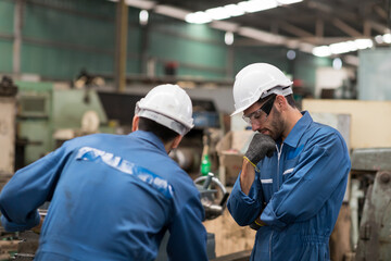 Two engineer male worker maintaining machine lathe metal at the industry factory. Group of Factory worker check or maintenance CNC machine in industry factory