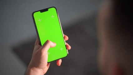 The man is using his phone in a vertical position. The green screen of the smartphone for chroma keying and tracking