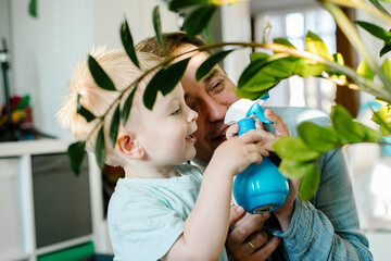 Happy little boy and man plash water on a home flower. Father dad and toddler son having fun.