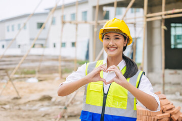 beauty woman hand love sign dressing as engineer worker builder in construction site background