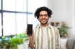 technology and people concept - smiling man in glasses showing smartphone with blank screen over home room background
