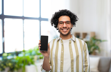 technology and people concept - smiling man in glasses showing smartphone with blank screen over home room background