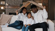 © Yuliia - African american family parents with daughter little girl adopted child sit on sofa under cardboard roof dreaming about own house relocation home insurance real estate buying flat kid protection