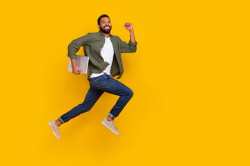 Full length photo of cute funky guy dressed green shirt jumping running modern gadget empty space isolated yellow color background