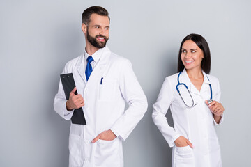 Wall Mural - Photo of smiling dreamy two doctors wear white coats writing prescription looking each other isolated grey color background