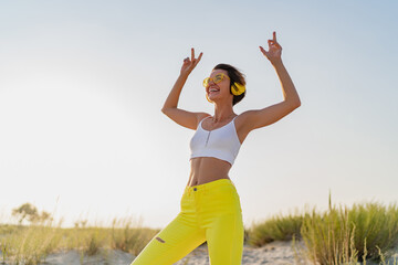 happy smiling woman listening to music in colorful yellow headphones on sunny beach in summer