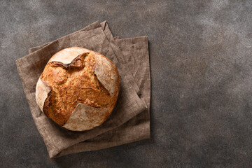 Loaf of freshly baked whole grain bread and barley spikelet on brown background. Top view. Copy space.