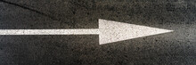 White Marking Of Arrow Form Located On Grey Asphalt Road Under Bright Sunlight On Summer Day Close Upper View