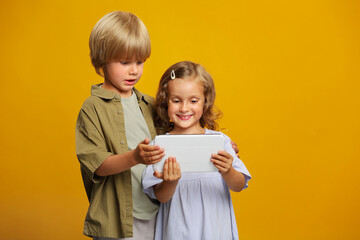 two kids using digital multimedia technologies, children standing with a tablet