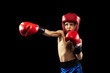 Dynamic portrait of sportive boy, kid in boxer gloves and shorts practicing isolated on dark background. Concept of sport, movement, studying, achievements, active lifestyle.