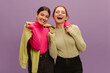 © Look! - Cheerful young european women laughing looking at camera on purple background. Brunette and redhead wear casual sweater and pants. People sincere emotions lifestyle concept.