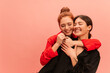 © Look! - Cute young caucasian girls with their eyes closed are standing in embrace on pink background with place for text. Brunette and redhead are wearing black and red shirt. Different emotions concept.