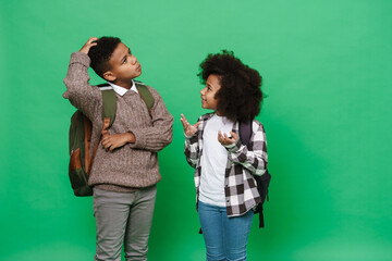 Two little african american kids with backpacks smiling and talking