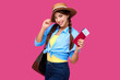 © khmelev - Smiling woman traveler in straw hat and backpack holding passport with plane ticket over pink isolate background