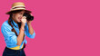© khmelev - Tourism concept. Happy smiling woman tourist in summer casual clothing holding photo camera and taking pictures, isolated on pink background with copy space
