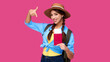 © khmelev - Young smiling girl with id card or passport holding airplane ticket, showing finger gesture on bright pink background. Caucasian woman in casual clothes and straw hat. Female european student