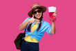 © khmelev - Smiling excited traveler woman showing vacation plane tickets and passport via finger gesture. Female tourist in sunglasses, summer casual clothes and straw hat over pink isolated background