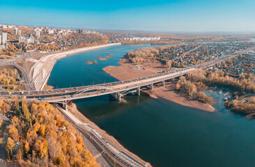 Wall Mural - Aerial cityscape view of city districts with automobile bridge over river in Ufa. Autumn parks with colorful trees