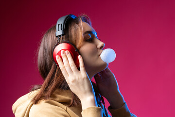 Wall Mural - Young beautiful fashionable hipster girl dressed in a hoodie  listening to music in red headphones in a studio red dramatic background