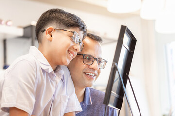 Wall Mural - Indian father and son choosing eyeglasses in optics store