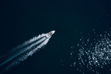 Wall Mural - Top view of a white boat sailing to the blue sea. Drone view of a boat sailing.Motor boat in the sea. Travel - image. Large white boat fast movement on blue water aerial view.