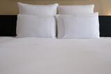 Fototapeta  - Clean Bedding sheets and pillow on natural wall room background. White bedding and pillow in a hotel room. White pillows on the empty bed.