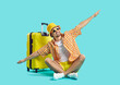 © Studio Romantic - Happy man who goes on summer vacation by air poses with suitcase on light blue background. Guy in summer clothes sits with outstretched arms imitating flight of airplane. Air flight journey concept.