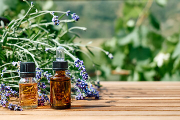 Bottles with natural essential lavender oil and fresh purple lavender flowers on wooden table against nature green background. Aromatherapy, alternative medicine and perfumery concept. Copy space.