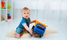 Cute Baby Is Sitting On The Floor Of The House, Playing With Colorful Educational Toys