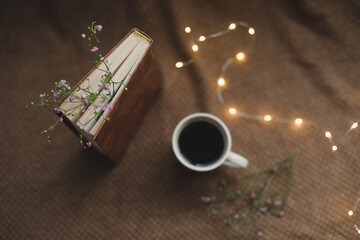 A book with flowers and cup of coffee on dark background top view