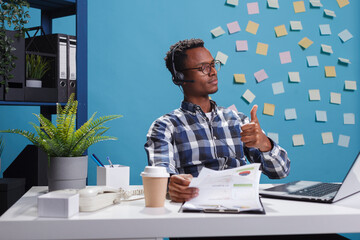 Wall Mural - helpline center operator wearing headset, showing thumbs up approval sign while on call with custome