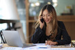 © Wasan - Asian businesswoman talking on mobile phone working on laptop in modern office. Happy business woman talking on mobile phone while analyzing weekly schedule in laptop.