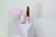 Lipstick on a white background with architecture shapes and pastel feathers. Close up on lipstick in deep nude color in in white packaging with cherry blossom