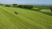 Tractor With Trailer Full Of Grass Driving On Green Field Hills In Yorkshire UK Countryside. Drone Aerial