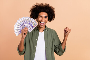 Portrait of attractive cheerful wavy-haired guy holding 100 bunch banknotes having fun isolated over beige pastel color background