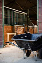 Plastic  Wheel Barrow In Front Of  Wooden Empty  Stable Barns On Horse Ranch
