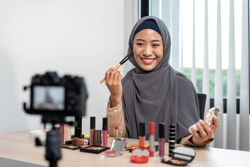 Wall Mural - Woman muslim blogger is present make up tutorial beauty cosmetic review product and broadcast live streaming video to teaching online on the camera screen at office studio