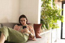 Non-binary Trans Woman Using Smartphone Lying On The Couch At Home