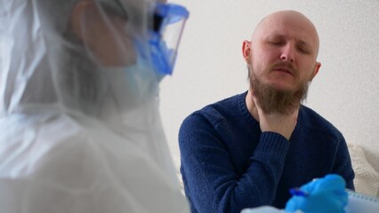 A sick man complains to the doctor about his health, the Man coughs and says that his throat hurts. A doctor in a protective suit, mask and goggles writes down the symptoms of the disease.